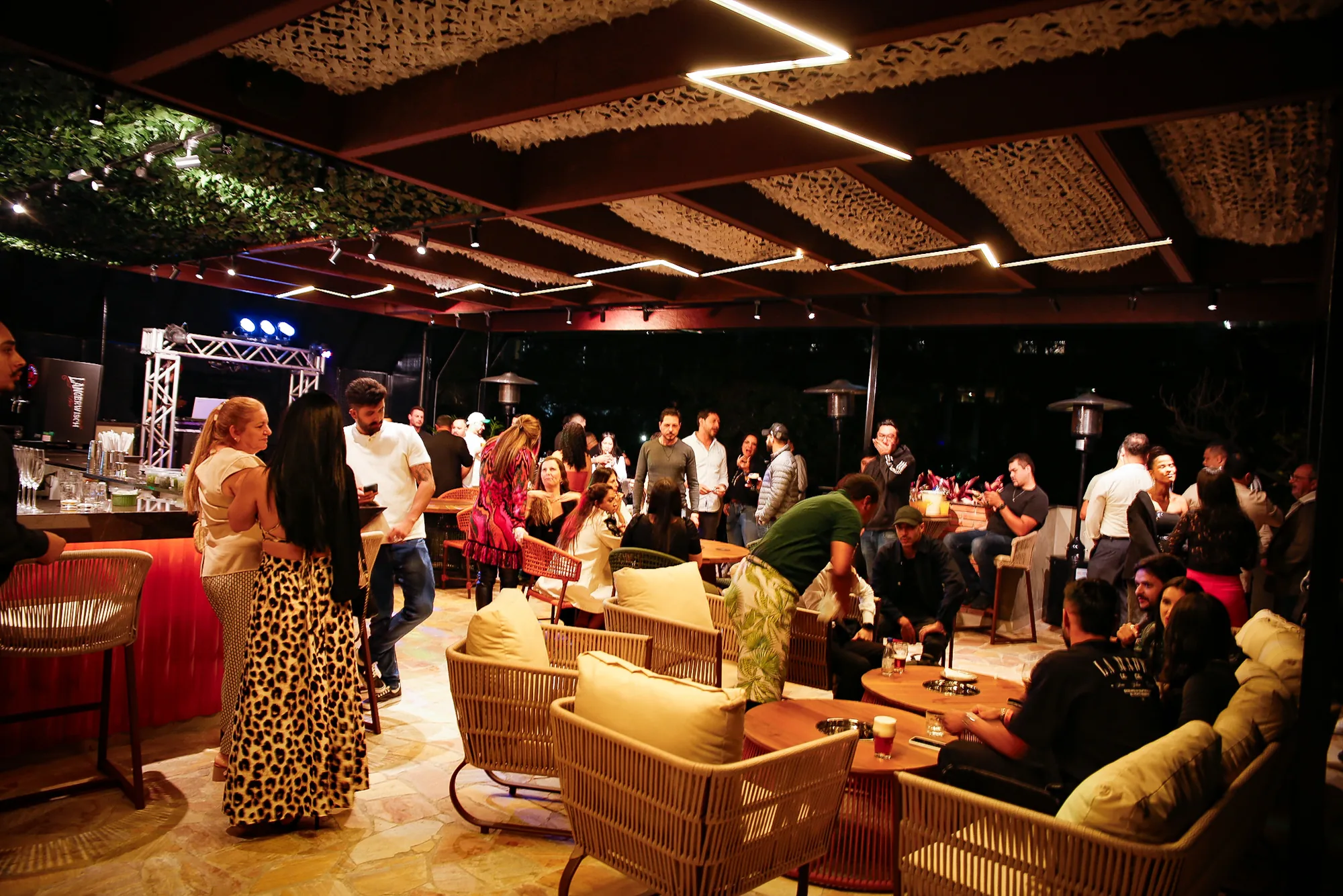 Rooftop do Perobah Pinheiros à noite, cheio, com convidados nos lounges e no bar.