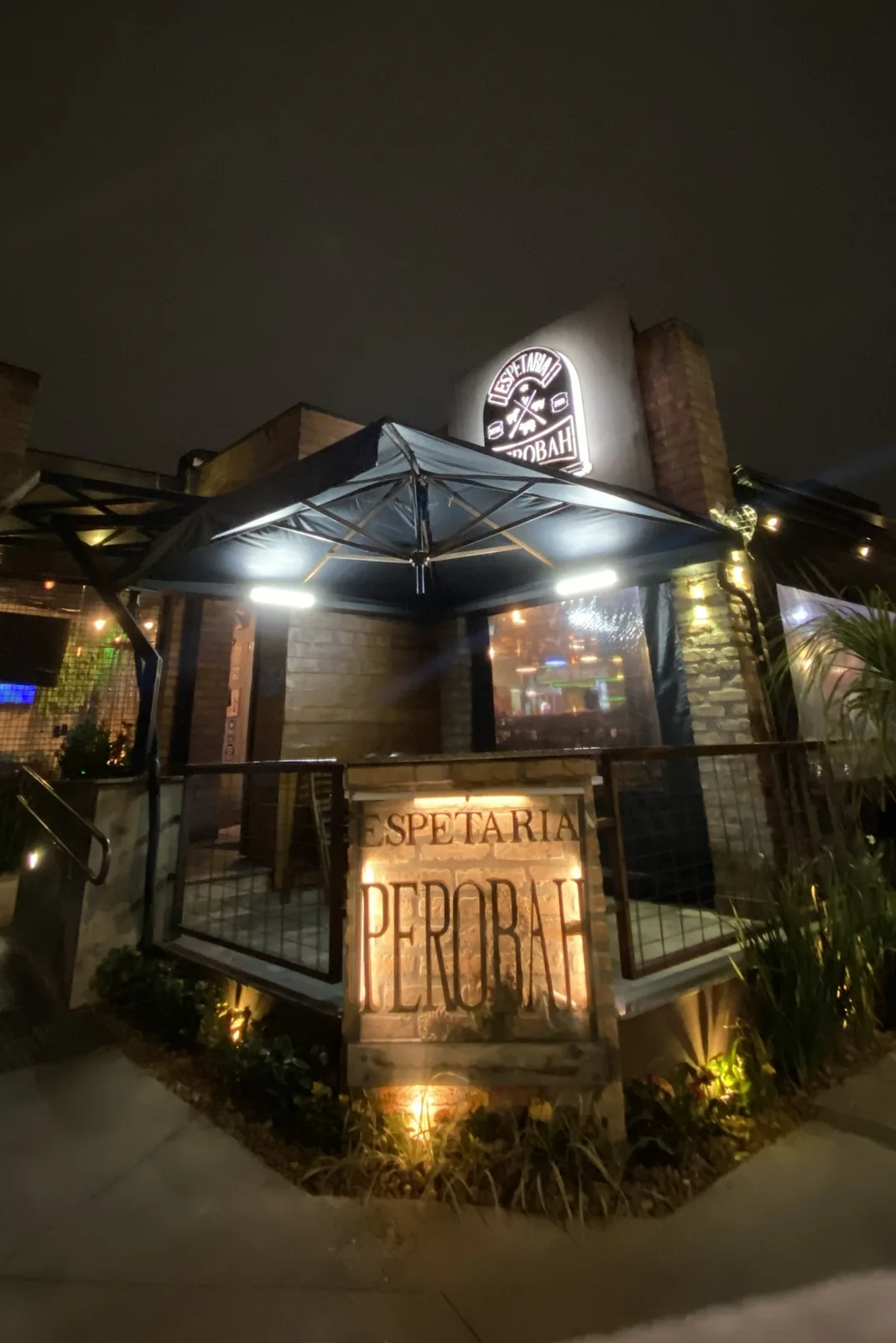 Entrada do Perobah à noite, com o letreiro iluminado e a placa de pedra na fachada.