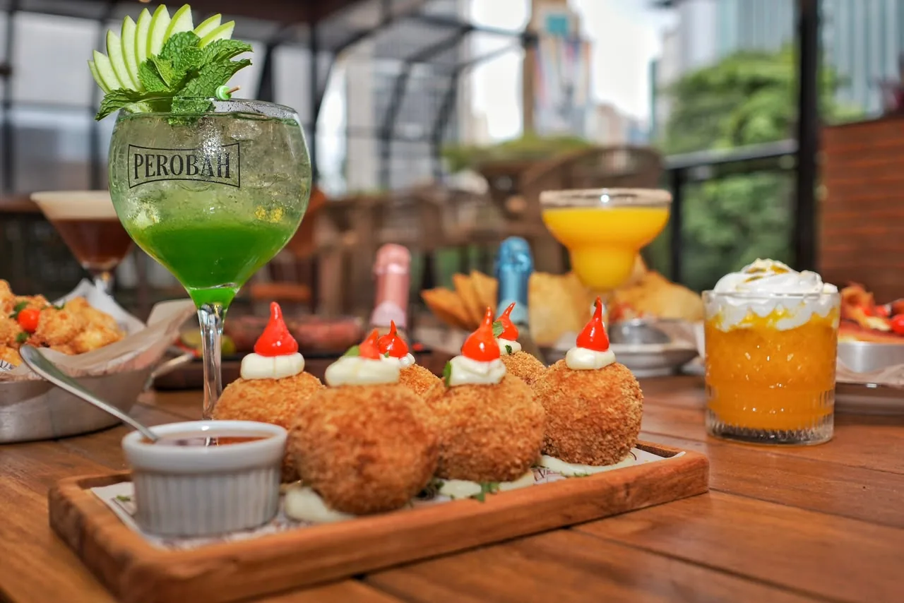 Mesa farta do Perobah, com porções e drinks servidos num copo com a marca da casa.